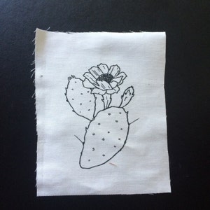 Peut inclure: Un dessin au trait noir et blanc d'un cactus de figue de Barbarie avec une fleur sur un fond de tissu blanc.