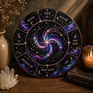May include: A round, black divination board with a celestial design. The center features a swirling galaxy of purple, blue, and pink hues. The board is segmented with phrases like "Yes," "Maybe," and "Not Now."
