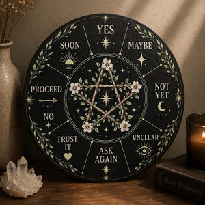 May include: A black divination board with floral accents and text including "YES," "MAYBE," and "ASK AGAIN." A pentagram design is at the center. The board is surrounded by a floral border. A candle and a book are in the background.