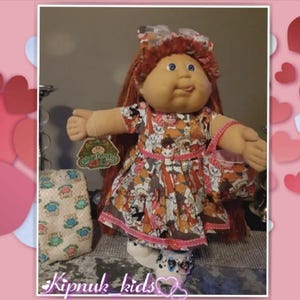 May include: A Cabbage Patch Kids doll with red hair, blue eyes, and a patterned dress. The doll is holding a matching purse and wearing shoes with a black and white pattern. A diaper and tag are also visible.