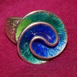 May include: A silver ring with a blue and green enamel design. The enamel is in a swirl pattern and the ring band is textured.