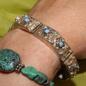 May include: A silver bracelet with turquoise stones and a silver and turquoise beaded bracelet on a person's wrist.
