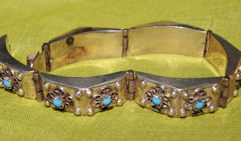 May include: Silver bracelet with a hinged clasp and turquoise stones set in filigree designs.