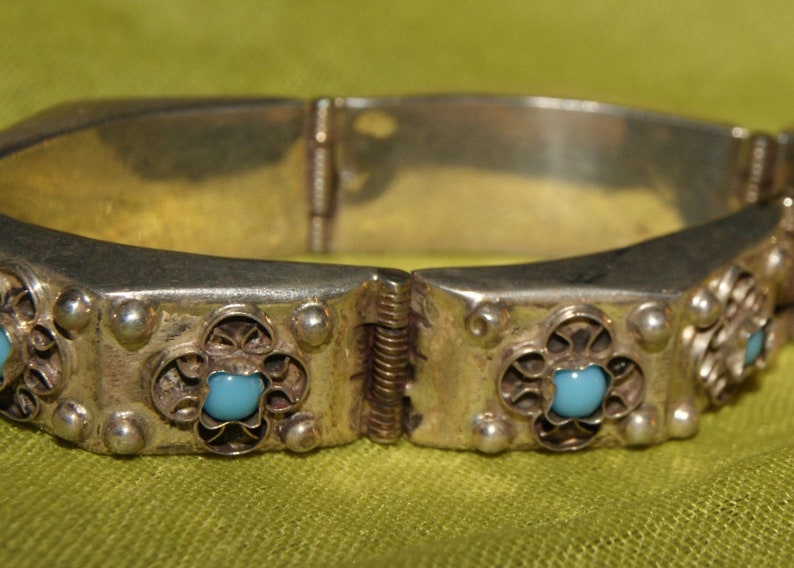 May include: Silver hinged bangle bracelet with a decorative design and turquoise blue stones.