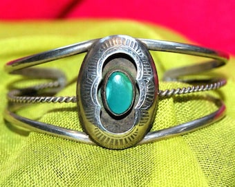 May include: A silver cuff bracelet featuring a central oval setting with a smooth turquoise stone. The metal surface displays etched radial patterns around the stone, while the band consists of two smooth outer wires and a twisted inner wire.