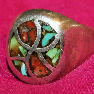 May include: A silver ring with a multi-colored stone inlay. The stone is set in a geometric pattern and features shades of turquoise, red, and brown.