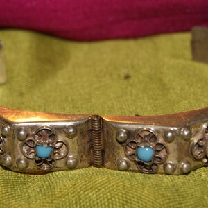 May include: A silver bracelet with a hinged clasp and blue turquoise stones set in ornate silver settings.