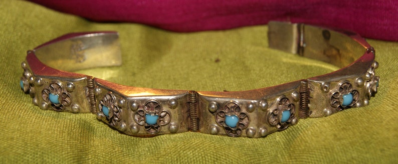 May include: A silver bracelet with a hinged clasp and blue turquoise stones set in ornate silver settings.