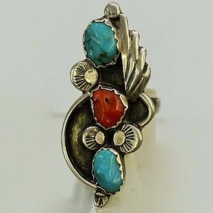 May include: A silver ring with turquoise and coral stones. The ring has a unique design with a curved band and a cluster of stones.