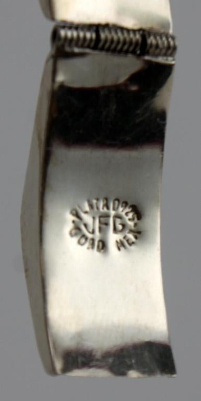 May include: Close-up of a silver bracelet with a textured design. The bracelet has a stamp that reads "Plata 925 JFD Oro Metal".