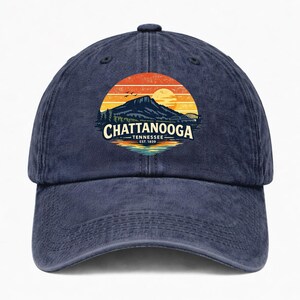 May include: A navy blue baseball cap featuring a circular graphic of a mountain landscape at sunset with the text CHATTANOOGA TENNESSEE EST. 1839. The design includes orange and yellow sky tones, a dark mountain silhouette, and water reflections.