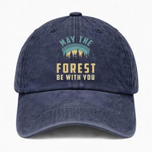 May include: A navy blue baseball cap with the text "MAY THE FOREST BE WITH YOU" in a forest-themed design. The cap features a curved brim and an adjustable strap for a comfortable fit. The design includes a forest silhouette.