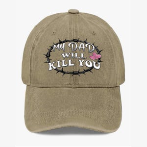 May include: A tan baseball cap with a curved brim. The cap features the text "MY DAD WILL KILL YOU" in white, surrounded by a barbed wire design, with two pink hearts.