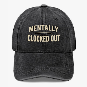 May include: A black denim baseball cap with the text "MENTALLY CLOCKED OUT" in a cream-colored font. The cap has a curved brim and an adjustable strap at the back. The hat is a casual accessory.