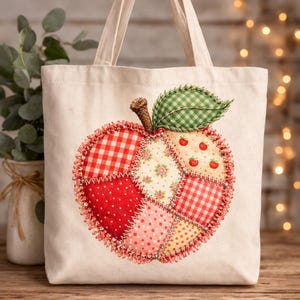 May include: A cream-coloured tote bag featuring an appliquéd apple design. The apple is made from fabric patches in red, pink, and yellow, with gingham, polka dot, and floral patterns. It has a brown stem and a green gingham leaf.