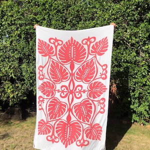 May include: A white fabric tapestry with a repeating pattern of pink stylized leaves. The leaves are arranged in a symmetrical design.