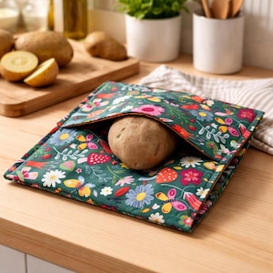 Puede incluir: Una bolsa de patatas verde con estampado floral que contiene una patata. La bolsa presenta un diseño colorido de flores, mariposas y setas. La bolsa está abierta, revelando la patata. La bolsa está sobre una superficie de madera.