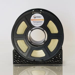 May include: A black spool of transparent PLA Performance 3D printing filament. The spool is labeled "ORGELY" and "Transparent." The filament is a light yellow color. The spool is held in a black honeycomb-patterned holder.