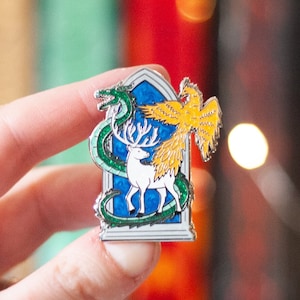 以下が含まれることがあります： 青いステンドグラスの枠の中に、緑のドラゴン、白い鹿、金色のフェニックスが描かれた銀色のエナメルピンです。