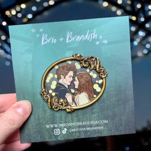 Puede incluir: Un pin con una pareja abrazándose, enmarcado en un marco dorado ornamentado. El pin está sobre una tarjeta verde azulado con el texto "Brio + Brandish" e información del sitio web. La pareja tiene cabello castaño y viste ropa formal.