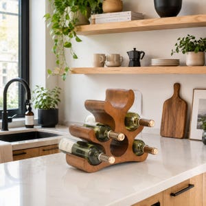May include: A brown wooden wine rack with a curved, organic shape designed to hold three glass bottles. The rack features three distinct circular cutouts for bottle placement, with two bottles currently resting in the lower and middle sections.