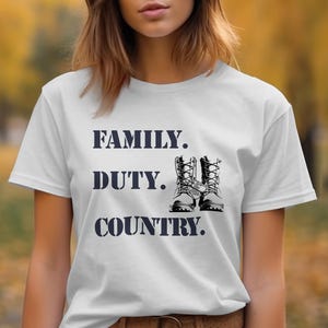 Puede incluir: Camiseta blanca con las palabras "FAMILY. DUTY. COUNTRY." en letras azul oscuro. Un par de botas militares en blanco y negro está impreso entre "DUTY." y "COUNTRY."