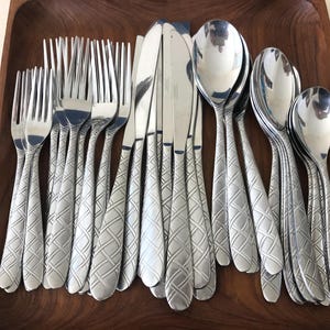 May include: A stainless steel flatware set featuring a repeating embossed lattice pattern on the handles. The collection includes multiple forks, knives, and spoons arranged together, showcasing a polished metallic finish and a consistent decorative design across all pieces.