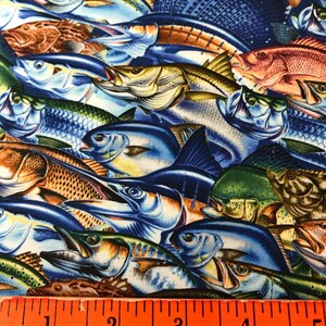 May include: A colorful fabric with a repeating pattern of various fish, including marlin, tuna, and snapper. The fabric is blue with a white background and features a ruler for scale.