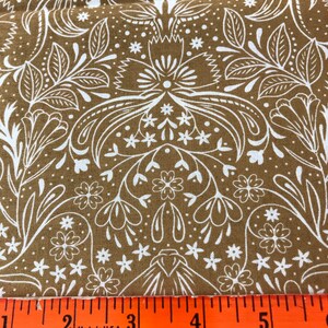 May include: Brown fabric with a white floral pattern. The fabric is measured with a ruler, showing 5 inches.