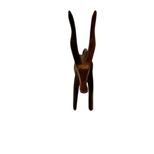 May include: A wooden antelope sculpture with long, curved horns. The sculpture is a dark brown color and has a smooth finish. The antelope is standing upright, with its head held high. The sculpture is likely a decorative item.