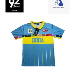 May include: A light blue short-sleeve polo shirt featuring a yellow collar and a horizontal yellow band across the chest with the word INDIA in blue letters. The shirt includes a multi-coloured chevron pattern, a Wills logo, and a circular emblem.
