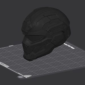 May include: A matte black tactical helmet with a geometric, multi-paneled design and a visor section, displayed as a 3D digital model on a grid-patterned build plate interface with visible software navigation icons and axis indicators.