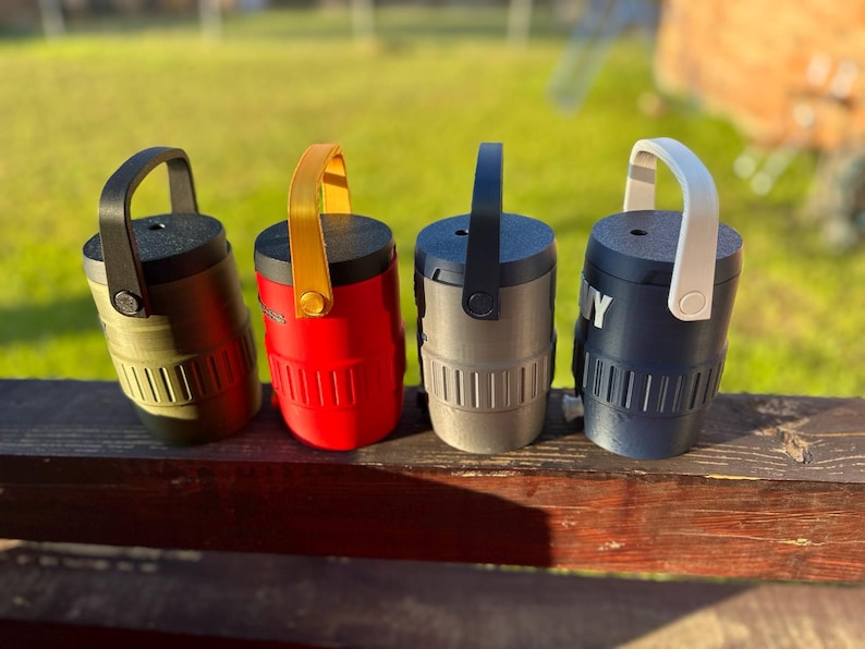 May include: Four cylindrical containers with handles in various colors: olive green, red, gray, and navy blue. Each container has a black top and a matching handle. The navy blue container has the word "NY" printed on it.