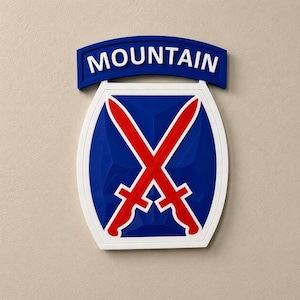May include: A wall-mounted emblem featuring a blue shield with two crossed red swords. Above the shield is a blue tab with the word MOUNTAIN in white capital letters. The entire design is outlined in white, creating a bold, dimensional appearance.