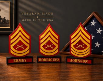 May include: Three red and yellow military rank insignias featuring crossed rifles, each mounted on a black base with a nameplate reading ERMEY, RODRIGUEZ, or JOHNSON. The text VETERAN MADE MADE IN THE USA is visible above the center insignia.