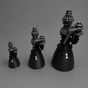 May include: Three matte black rocket engine models of varying sizes, each featuring a complex upper mechanical assembly and a wide, conical nozzle. Each engine is marked with a white number 1 on the side of the nozzle, showcasing intricate details.