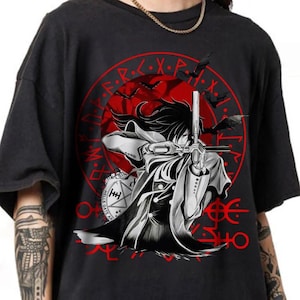 May include: Black t-shirt featuring a detailed anime-style illustration. The design includes a character aiming a weapon, set against a red circular backdrop with text and bats. The shirt has a vintage, slightly faded appearance.