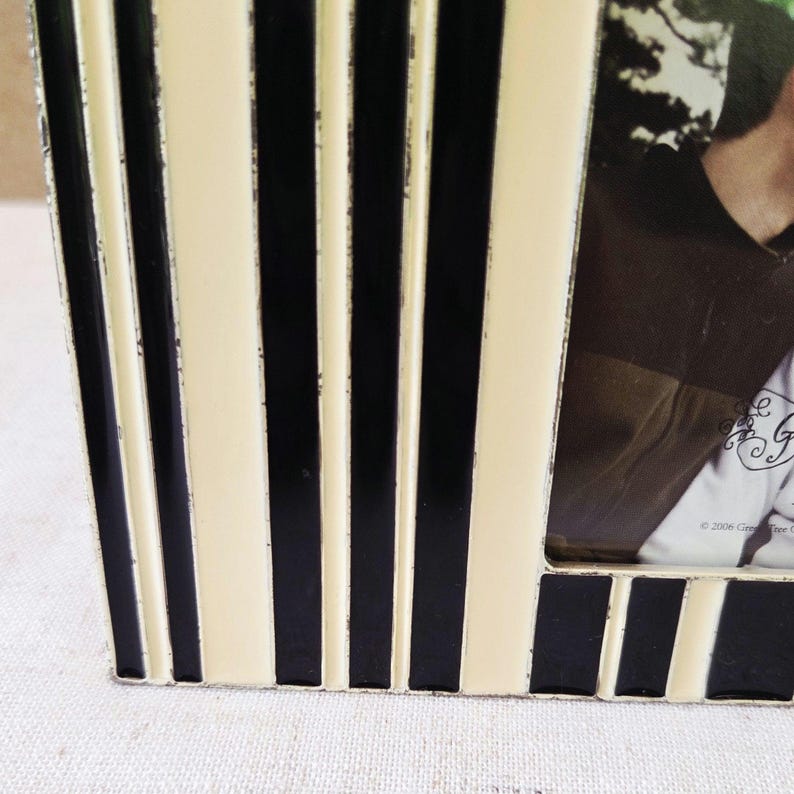 May include: A close-up of a black and cream-colored striped photo frame. The frame has a rectangular shape with vertical stripes. The frame is made of metal and has a distressed finish.