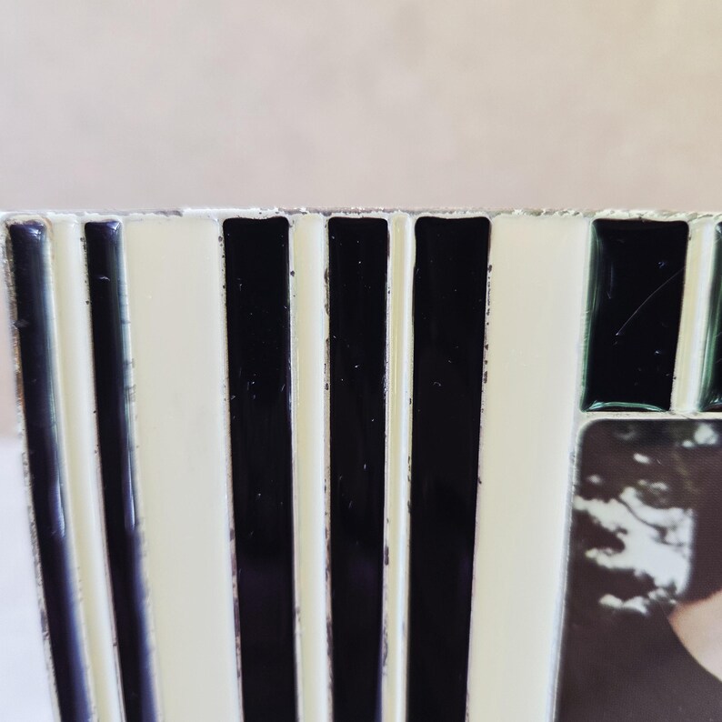 May include: Close-up of a black and white striped picture frame. The frame has alternating vertical stripes of black and white. The frame is made of a glossy material and has a rectangular shape. The frame is designed to hold a photograph.