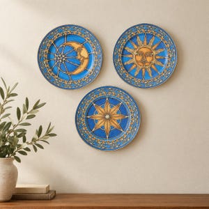 May include: Three circular decorative plates featuring celestial motifs in shades of blue and gold. One plate displays a crescent moon, another a radiant sun, and the third a central star. Each plate has a detailed border with gold accents.