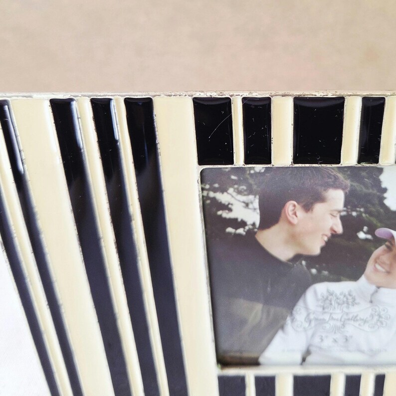 May include: A decorative photo frame with a black and cream striped design. The frame holds a photograph of two people. The frame's design features vertical stripes and a rectangular opening for the photo.