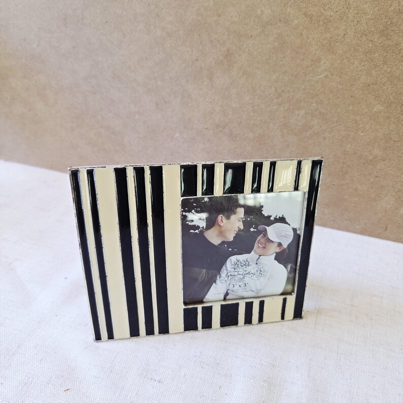 May include: A black and cream striped photo frame with a photograph of two people. The frame has a rectangular shape with a slightly angled design. The photograph is in black and white.