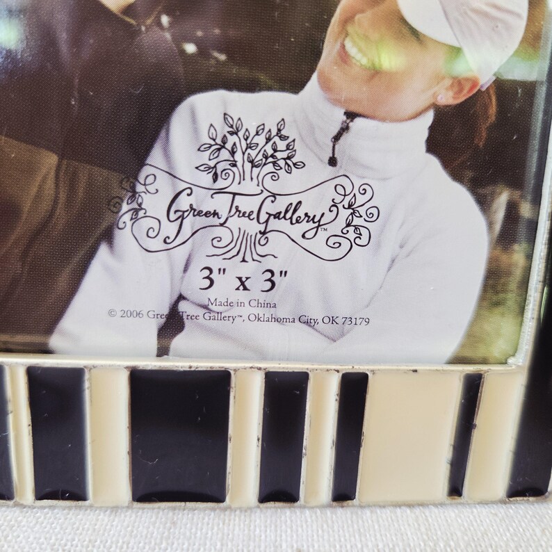 May include: A decorative photo frame with a black, white, and cream-colored striped border. The frame is designed to hold a 3-inch by 3-inch photo. The text "Green Tree Gallery" is visible, along with the dimensions and manufacturing information.