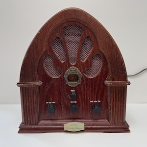 May include: A vintage-style wooden radio with a brown wood finish. The radio has a speaker grille with a decorative design and several knobs for tuning, volume, and tone. The radio has a label that reads "Lloyd's Collector's Edition".