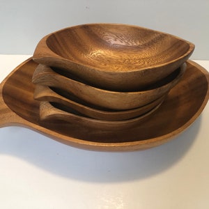 May include: Set of four wooden bowls, nested together. The bowls are made of light brown wood and have a smooth, rounded shape. The bowls are ideal for serving snacks, dips, or salads.