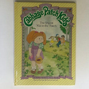May include: A vintage Cabbage Patch Kids storybook titled "The Shyest 'Kid in the 'Patch." The cover shows a Cabbage Patch Kid with red hair and a purple dress, holding a basket. Other children are playing in a field, with text below.