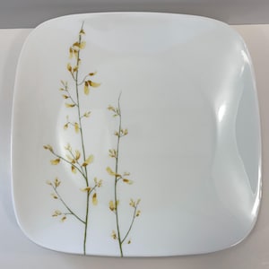 May include: White square plate with rounded corners. The plate has a delicate floral design with yellow and brown accents. The design features slender stems with small leaves and seed pods. The plate has a clean, modern aesthetic.