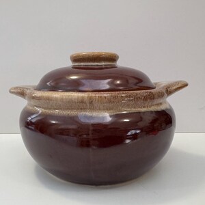 May include: A brown glazed ceramic casserole dish with a lid. The dish has a white rim and a light brown glaze on the lid.