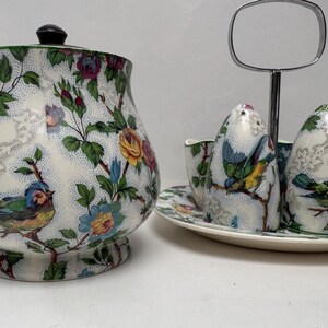May include: A white ceramic sugar bowl with a lid and floral pattern, a matching creamer, and two salt and pepper shakers with a bird design. The set is on a white ceramic tray with a floral pattern.