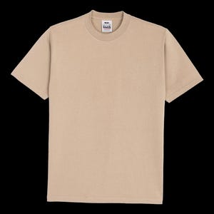 Könnte beinhalten: Ein einfarbiges, beiges Kurzarm-T-Shirt mit Rundhalsausschnitt. Das Kleidungsstück verfügt über ein sichtbares weißes Innenetikett am Kragen mit dem in Schwarz gedruckten Text Pro Club. Das T-Shirt ist mit einem Standard-Saum an Ärmeln versehen.
